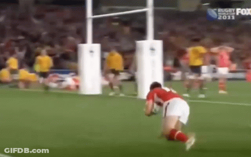 A Man Is Kneeling Down On A Soccer Field With A Rugby Ball . GIF