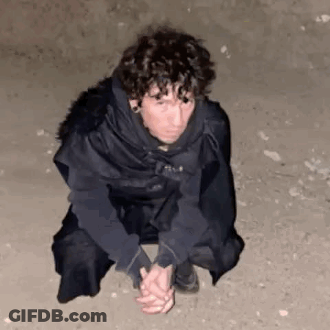 A Man Is Kneeling Down On The Ground With His Hands Folded . GIF