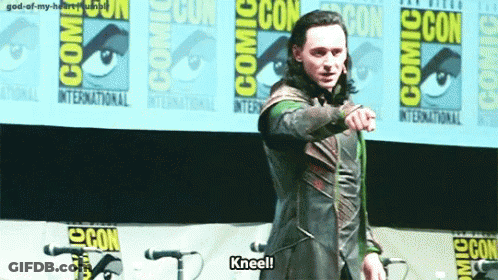 A Man Is Kneeling In Front Of A Comic Con Banner . GIF