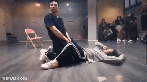 A Man Is Kneeling Over A Woman Laying On The Floor In A Dance Studio . GIF