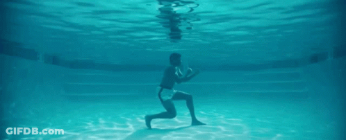 A Man Is Kneeling Underwater In A Swimming Pool . GIF