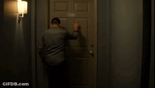 A Man Is Knocking On A Door In A Hallway . GIF