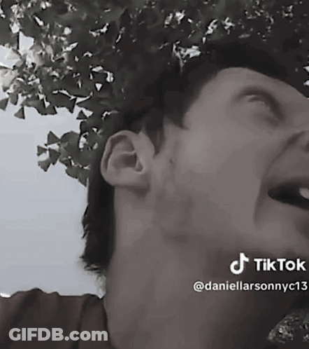 A Man Is Laughing In A Black And White Photo With A Tree In The Background . GIF