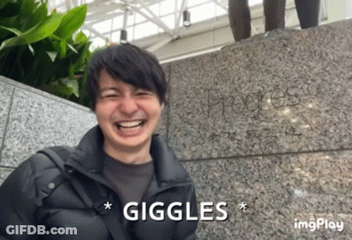 A Man Is Laughing In Front Of A Stone Wall And The Word Giggles Is Above Him GIF