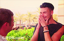 A Man Is Laughing While A Woman Covers His Mouth With Her Hands . GIF