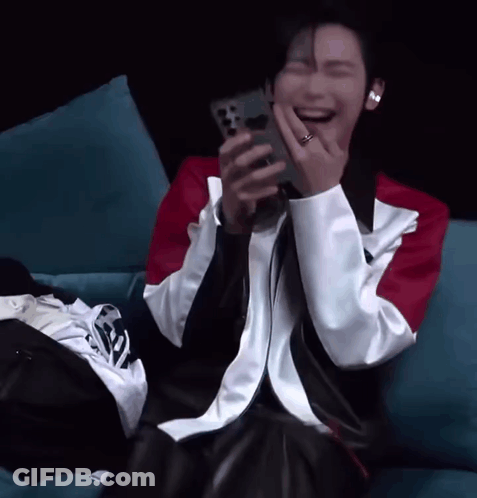 A Man Is Laughing While Holding A Cell Phone In His Hand GIF