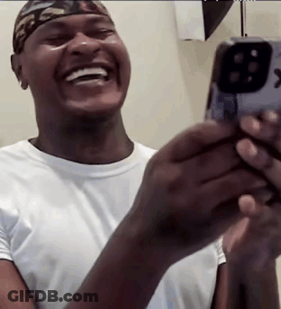 A Man Is Laughing While Holding A Cell Phone In His Hands . GIF