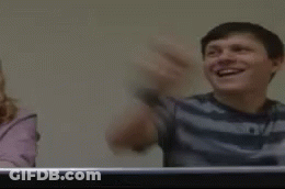 A Man Is Laughing With His Arms In The Air While Sitting At A Table . GIF