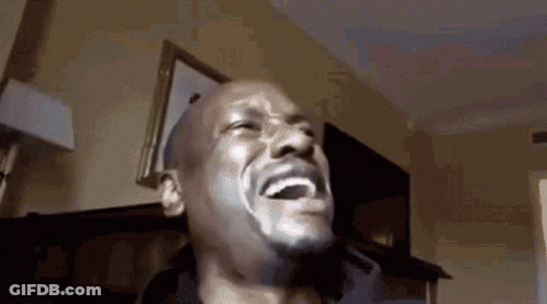 A Man Is Laughing With His Mouth Open And His Eyes Closed In A Room . GIF