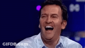 A Man Is Laughing With His Mouth Open While Wearing A Blue Shirt . GIF
