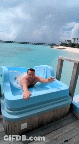 A Man Is Laying In A Blue Tub On A Dock Overlooking The Ocean GIF