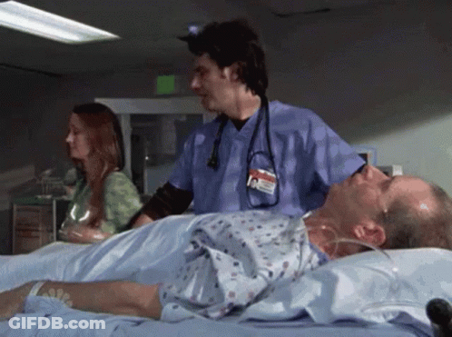 A Man Is Laying In A Hospital Bed While A Nurse Stands Behind Him . GIF