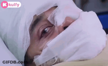A Man Is Laying In A Hospital Bed With A Bandage On His Head And Face . GIF