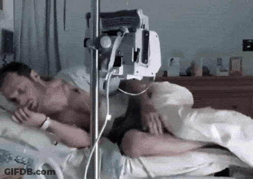 A Man Is Laying In A Hospital Bed With An Iv In His Arm GIF
