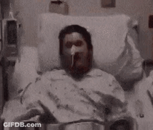 A Man Is Laying In A Hospital Bed With An Oxygen Mask On . GIF