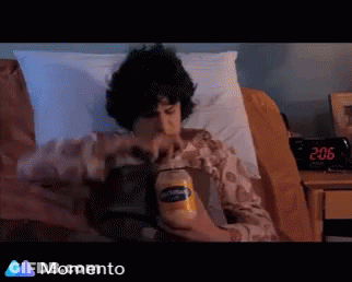 A Man Is Laying In Bed Holding A Bottle Of Peanut Butter GIF