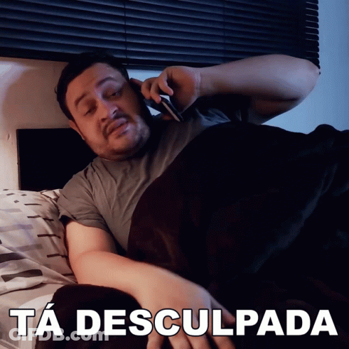 A Man Is Laying In Bed Talking On A Cell Phone With The Caption Ta Desculpada Above Him GIF
