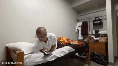 A Man Is Laying On A Bed In A Room With A Bag That Says Tour GIF
