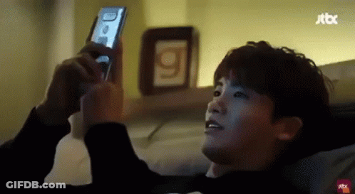 A Man Is Laying On A Bed Using A Cell Phone . GIF
