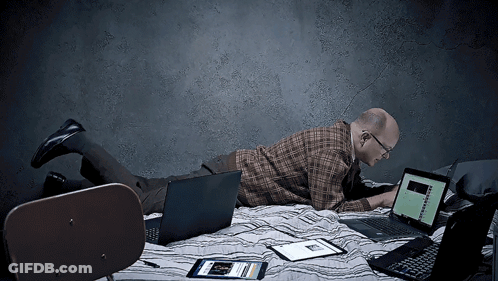 A Man Is Laying On A Bed Using A Laptop And A Tablet GIF