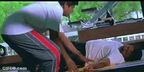 A Man Is Laying On A Bed While Another Man Is Standing Next To Him . GIF