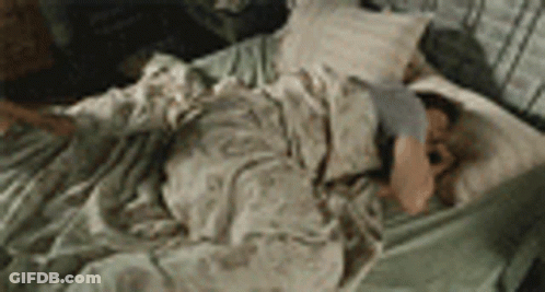 A Man Is Laying On A Bed With A Blanket And Pillow . GIF