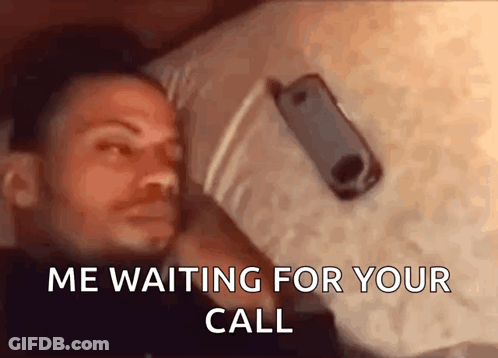 A Man Is Laying On A Bed With A Cell Phone In His Hand And The Words " Me Waiting For Your Call " Above Him GIF