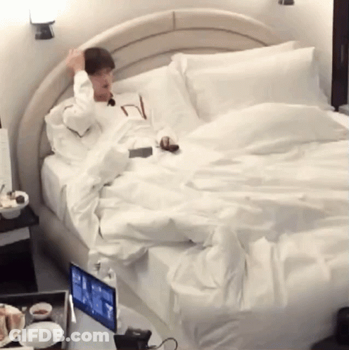 A Man Is Laying On A Bed With A Laptop On It GIF