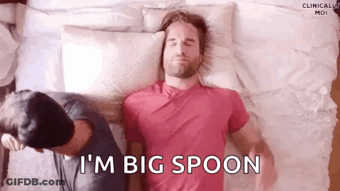 A Man Is Laying On A Bed With A Pillow On His Head And Another Man Is Standing Behind Him . GIF