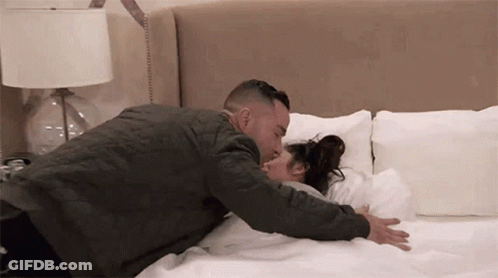 A Man Is Laying On A Bed With A Woman And Kissing Her . GIF