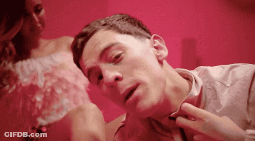 A Man Is Laying On A Bed With A Woman In A Pink Dress Behind Him GIF