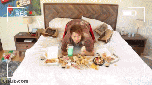 A Man Is Laying On A Bed With Boxes Of Food And A Sign That Says Office Entrance On The Wall Behind Him GIF