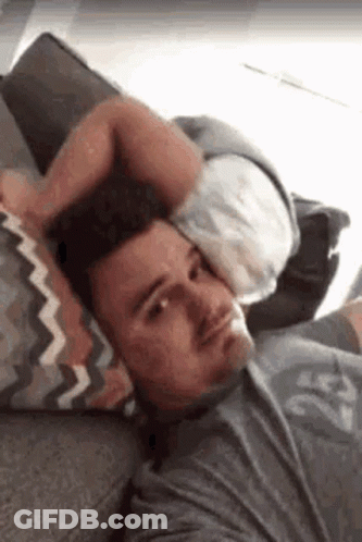 A Man Is Laying On A Couch Holding A Pillow Over His Head . GIF