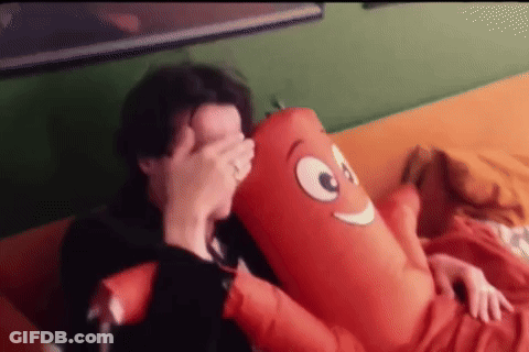 A Man Is Laying On A Couch Holding A Stuffed Sausage GIF