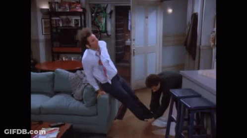 A Man Is Laying On A Couch While Another Man Holds His Legs Up In The Air . GIF