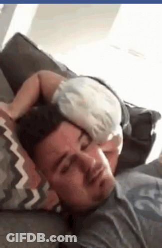 A Man Is Laying On A Couch With A Baby Sleeping On His Head . GIF