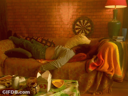 A Man Is Laying On A Couch With A Dart Board In The Background GIF