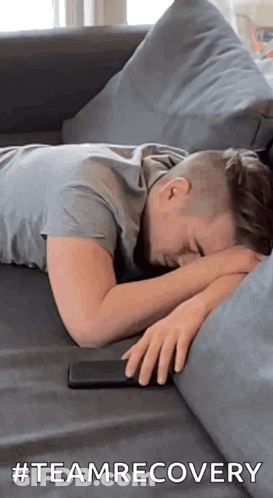 A Man Is Laying On A Couch With His Head On His Hands And A Cell Phone . GIF