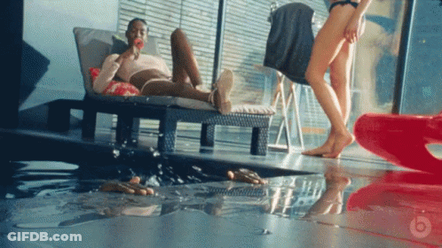 A Man Is Laying On A Lounge Chair Eating A Lollipop While A Woman Walks By GIF
