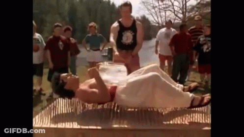A Man Is Laying On A Mattress Made Of Nails While A Group Of People Watch . GIF