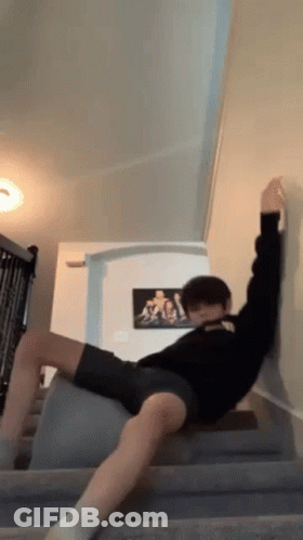 A Man Is Laying On A Staircase With His Legs Crossed And A Picture Of A Man On The Wall Behind Him . GIF