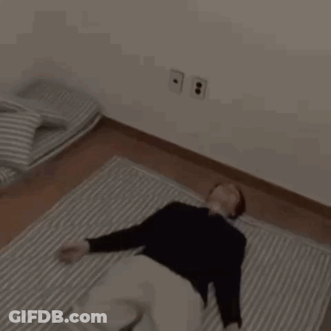 A Man Is Laying On A Striped Blanket On The Floor GIF