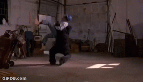 A Man Is Laying On His Back In A Garage While Another Man Looks On . GIF