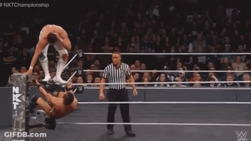 A Man Is Laying On His Back In A Wrestling Ring While Another Man Kicks Him . GIF