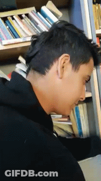 A Man Is Laying On His Back In Front Of A Bookshelf Filled With Books . GIF