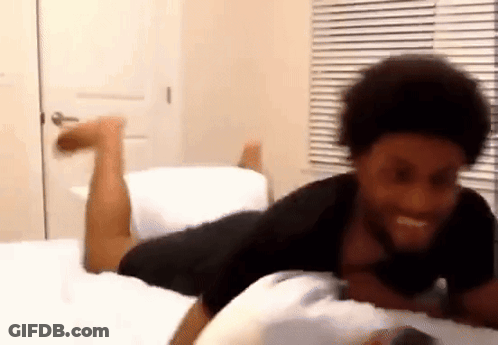 A Man Is Laying On His Stomach On A Bed With His Legs Up . GIF