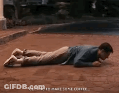 A Man Is Laying On His Stomach On A Brick Sidewalk Drinking Coffee . GIF