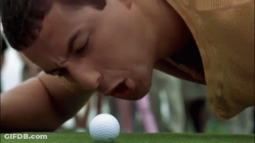 A Man Is Laying On His Stomach On A Golf Course Looking At A Golf Ball . GIF
