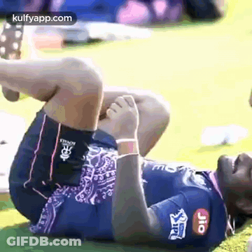 A Man Is Laying On His Stomach On The Grass And Stretching His Leg . GIF