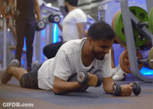 A Man Is Laying On The Floor Lifting Dumbbells GIF